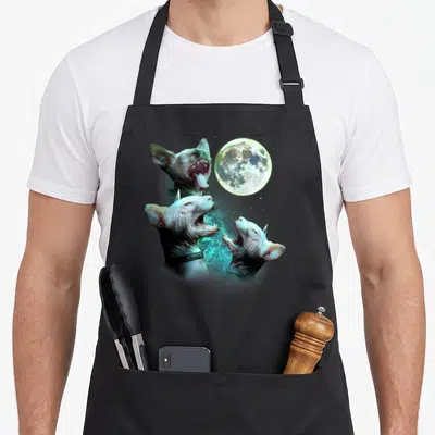 Three cat apron - Three hairless sphynx cats howling at a moon with pink blue and grey tones — shown on a black cotton canvas apron against a white background