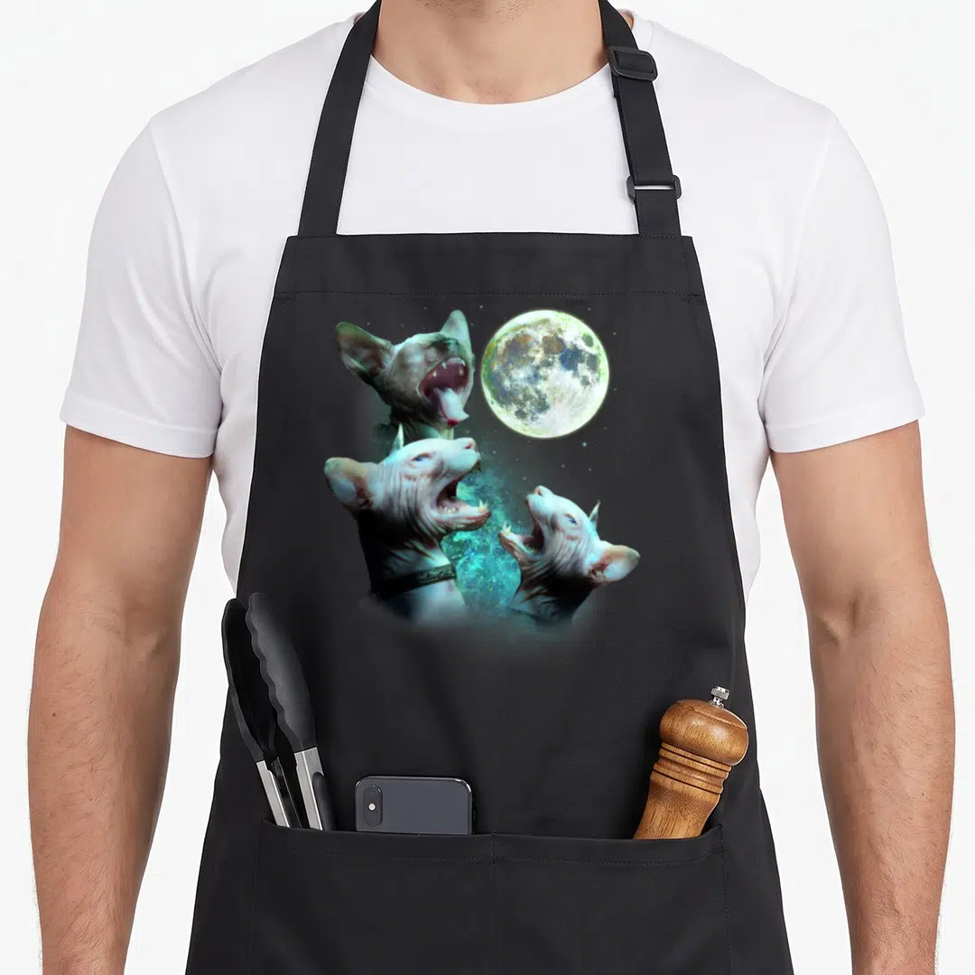 Three cat apron - Three hairless sphynx cats howling at a moon with pink blue and grey tones — shown on a black cotton canvas apron against a white background