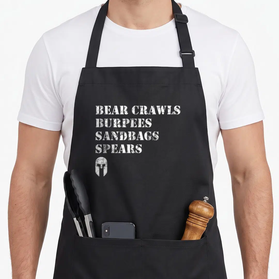 Crawl bear apron - White distressed text reading Bear Crawls Burpees Sandbags Spears above a Spartan helmet icon — shown on a black cotton canvas apron against a white background