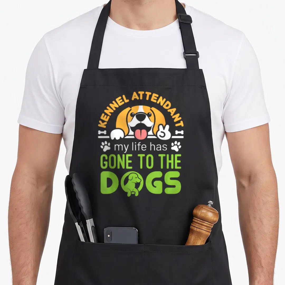 Kennel dog apron - Cartoon dog head with KENNEL ATTENDANT text and GONE TO THE DOGS slogan in orange and green — shown on a black cotton canvas apron against a white background