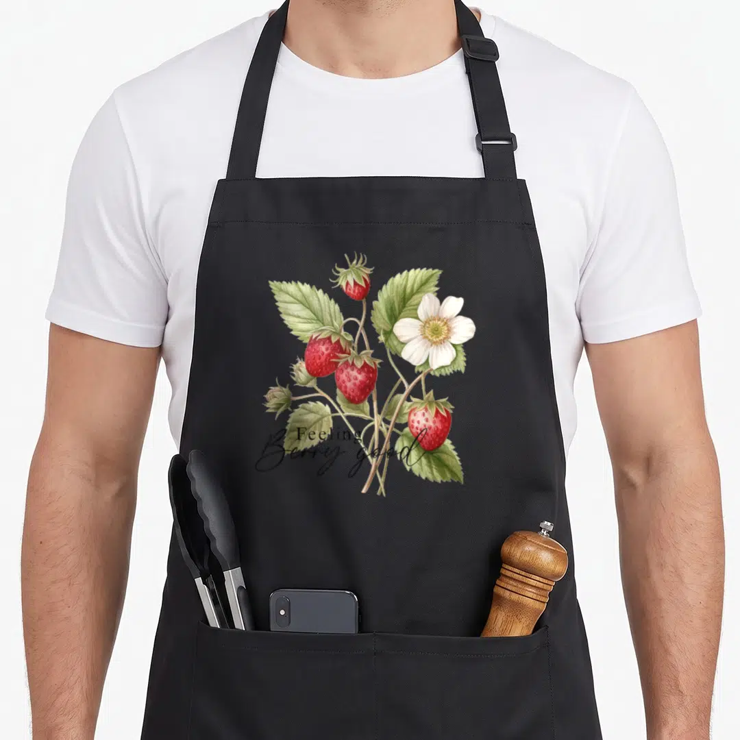 Strawberry floral apron - Botanical strawberry plant with red berries and Feeling Berry good text — shown on a black cotton canvas apron against a white background