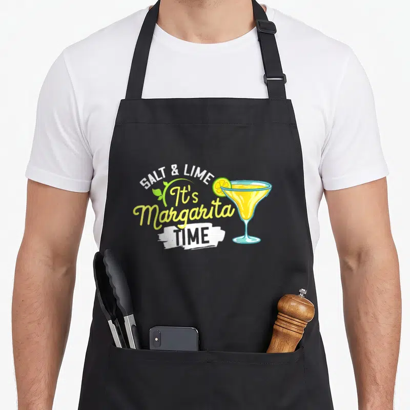 Cute margarita apron - SALT & LIME text next to a yellow margarita glass with green leaves — shown on a black cotton canvas apron against a white background