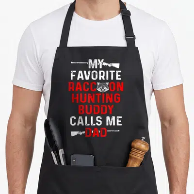 Buddy hunter apron - Stacked white and red text reading My Favorite Raccoon Hunting Buddy Calls Me Dad with a raccoon — shown on a black cotton canvas apron against a white background