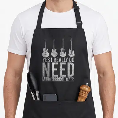 These funny string apron - Four distressed white guitars above stacked text reading YES I REALLY DO NEED ALL THESE — shown on a black cotton canvas apron against a white background