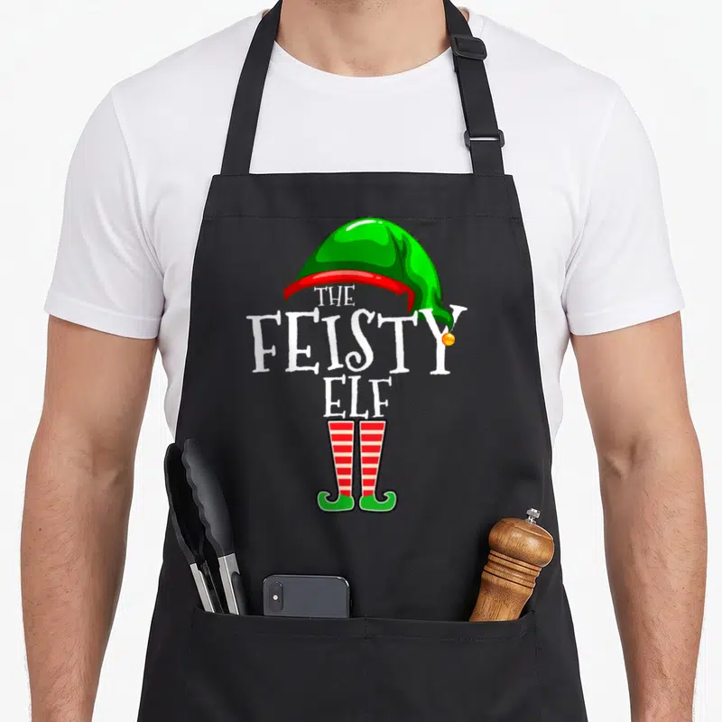 Feisty personalized family aprons - White text reading The Feisty Elf with green hat and red striped legs in cartoon — shown on a black cotton canvas apron against a white background