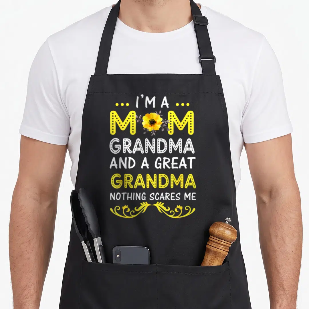 Grandma mother's day aprons - Stacked yellow and white text reading I'm a mom grandma and great grandma nothing scares — shown on a black cotton canvas apron against a white background