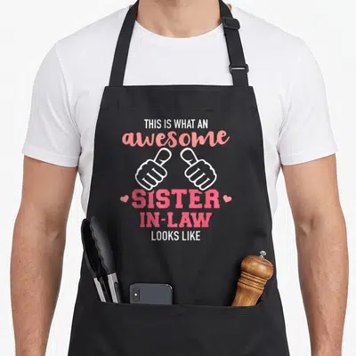 Funny sister in law apron - Pink and white text with two thumbs up hands and hearts celebrating a sister in law — shown on a black cotton canvas apron against a white background