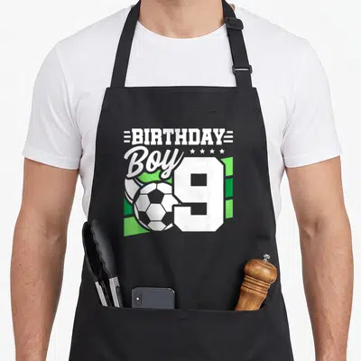 Soccer 9th birthday apron - BIRTHDAY Boy 9 text with soccer ball and green geometric shapes — shown on a black cotton canvas apron against a white background