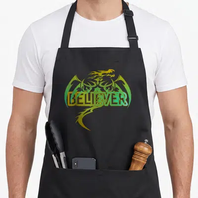Original dragon apron - BELIEVER text over yellow and green cartoon dragon head and tail — shown on a black cotton canvas apron against a white background