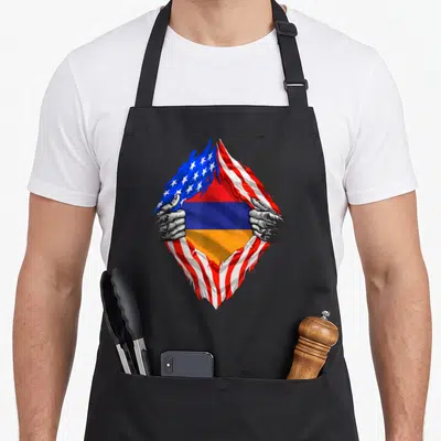 Armenia armenian american flag apron - Two grey hands rip open a USA flag revealing Armenian red blue and orange stripes — shown on a black cotton canvas apron against a white background