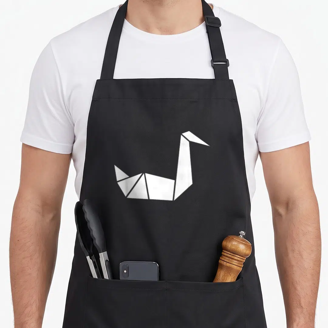 Swan origami apron - Minimalist white origami crane centered on grey background — shown on a black cotton canvas apron against a white background