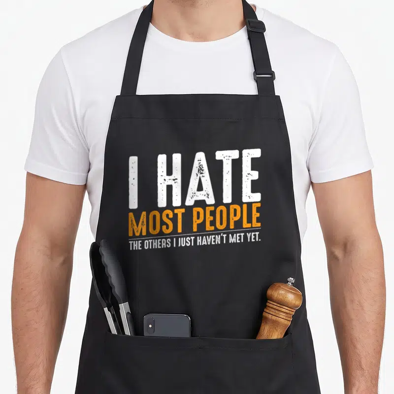 Most people sarcasm apron - Distressed white and orange text reading I HATE MOST PEOPLE THE OTHERS I JUST HAVEN'T MET — shown on a black cotton canvas apron against a white background