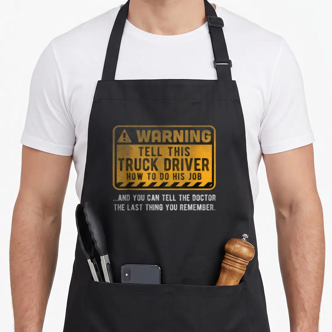 Warning truck apron - Yellow warning sign with black text and white slogan below reading about truck drivers — shown on a black cotton canvas apron against a white background