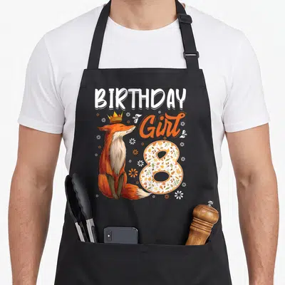 8th fox aprons - Crowned fox sitting next to BIRTHDAY Girl 8 text with floral number 8 and scattered flowers — shown on a black cotton canvas apron against a white background