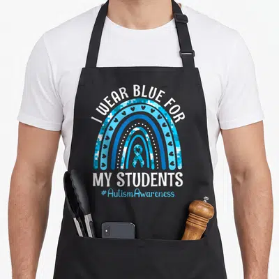 Student teacher art apron - I WEAR BLUE FOR MY STUDENTS rainbow with puzzle pieces and autism ribbon — shown on a black cotton canvas apron against a white background