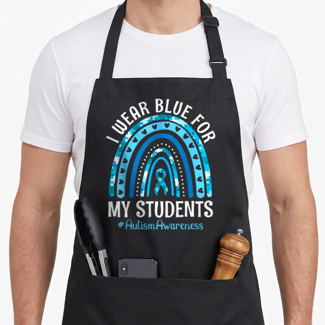Student teacher art apron - I WEAR BLUE FOR MY STUDENTS rainbow with puzzle pieces and autism ribbon — shown on a black cotton canvas apron against a white background