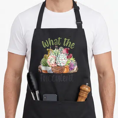 Fucculent gardening cactus apron - Watercolor succulents in pots with arched text What the and Fucculent below — shown on a black cotton canvas apron against a white background