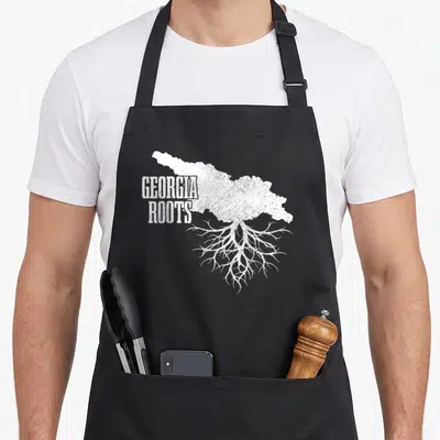 Map patriotic apron - Distressed white Georgia state map with roots and text GEORGIA ROOTS — shown on a black cotton canvas apron against a white background