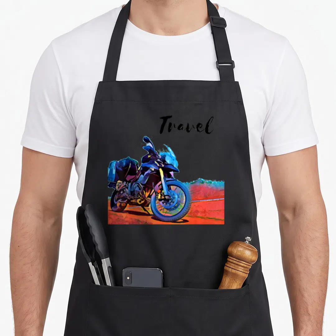 Motorcycle travel bike apron - Script Travel text above a blue motorcycle parked on red earth — shown on a black cotton canvas apron against a white background