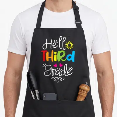 Third hello apron - Stacked Hello Third Grade text with sun, hearts, and swirl in rainbow colors — shown on a black cotton canvas apron against a white background