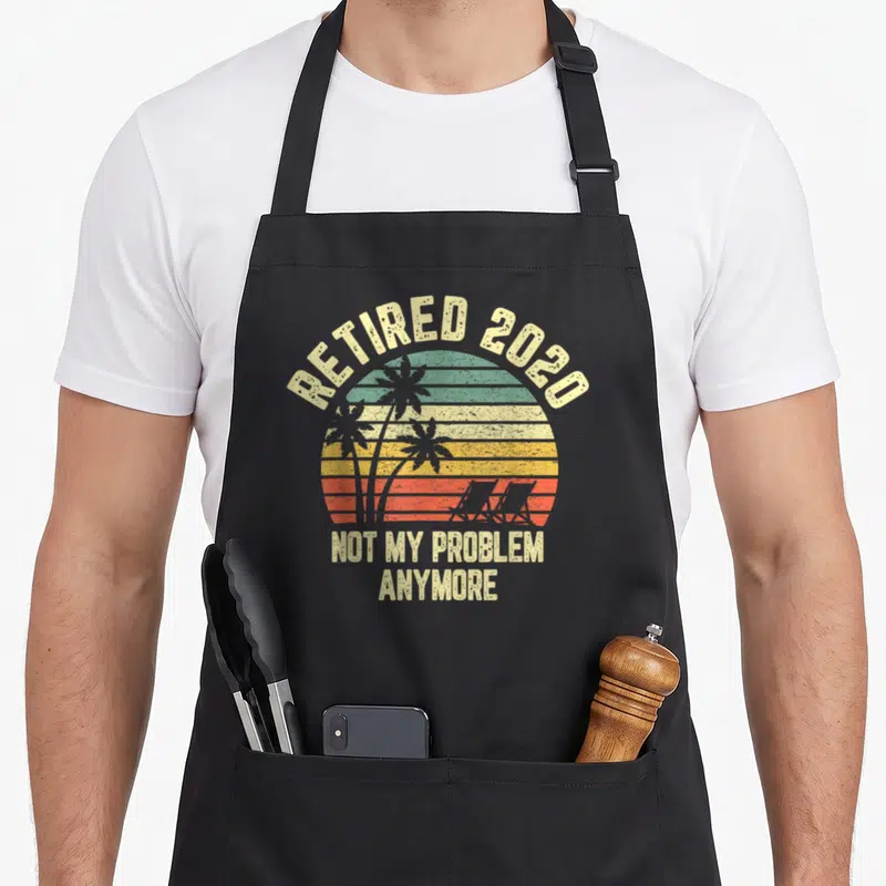 Retired problem retirement apron - Retro striped sunset with palm trees and text reading Retired 2020 Not My Problem — shown on a black cotton canvas apron against a white background