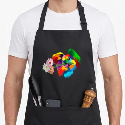 Colored dog apron - Rainbow cartoon papillon head holding three daisies in mouth — shown on a black cotton canvas apron against a white background