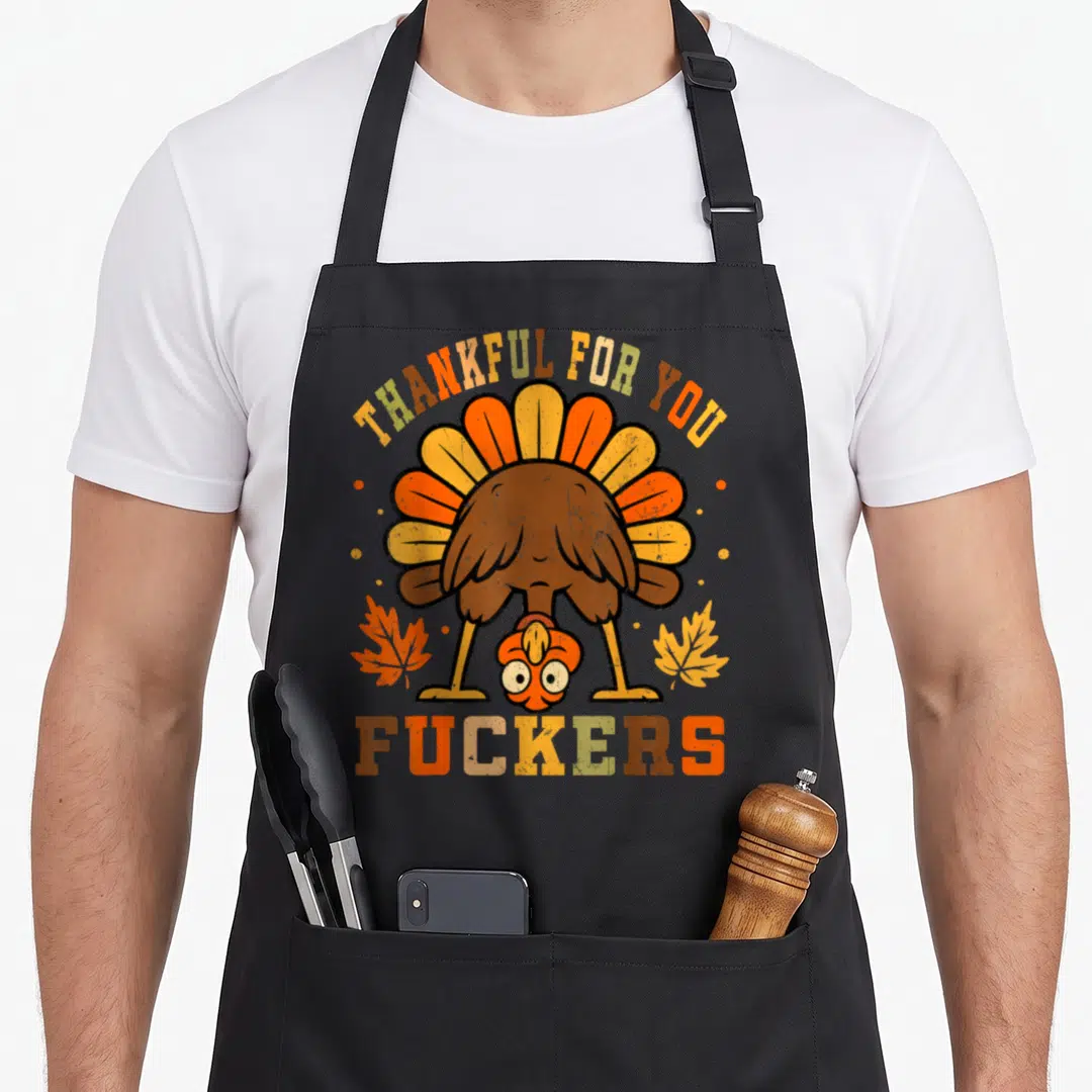 Funny thanksgiving thankful apron - Upside down turkey illustration with THANKFUL FOR YOU FUCKERS text in retro autumn — shown on a black cotton canvas apron against a white background