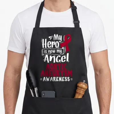 Aortic ribbon apron - My Hero is now my Angel Aortic Aneurysm Awareness red ribbon typography — shown on a black cotton canvas apron against a white background