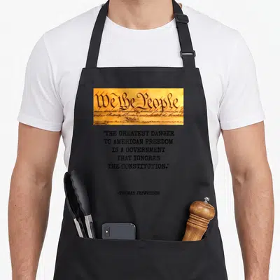 Greatest star quotes apron - We the People parchment strip above stacked Thomas Jefferson quote about government — shown on a black cotton canvas apron against a white background