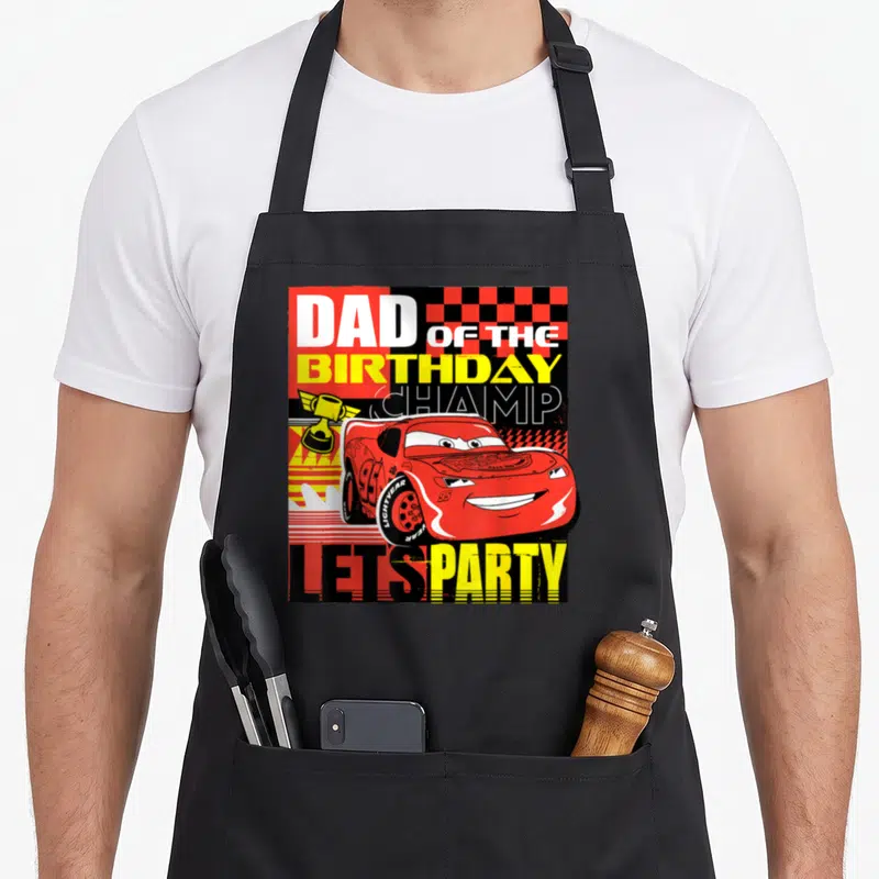 Birthday champ car apron - Red cartoon race car with gold trophy and checkered background under bold birthday party text — shown on a black cotton canvas apron against a white background