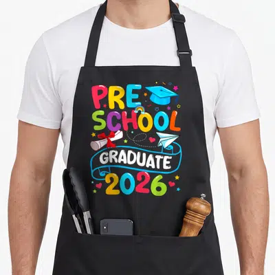 Grad preschool apron - PRE SCHOOL GRADUATE 2026 text with blue cap, red scroll, paper plane, and rainbow in cartoon — shown on a black cotton canvas apron against a white background