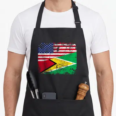 Guyanese american flag apron - Distressed merged US and Guyana flag print in red white blue green and yellow — shown on a black cotton canvas apron against a white background