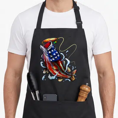 Blue patriotic aprons - Jumping fish with US flag pattern body and fishing lure in red white blue yellow cartoon style — shown on a black cotton canvas apron against a white background