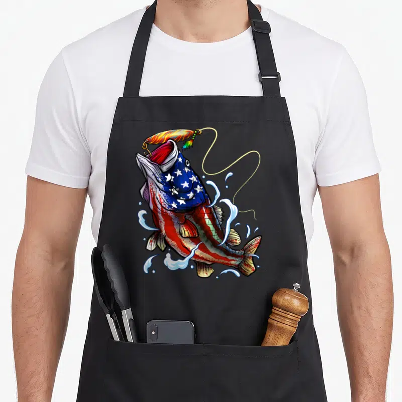 Blue patriotic aprons - Jumping fish with US flag pattern body and fishing lure in red white blue yellow cartoon style — shown on a black cotton canvas apron against a white background