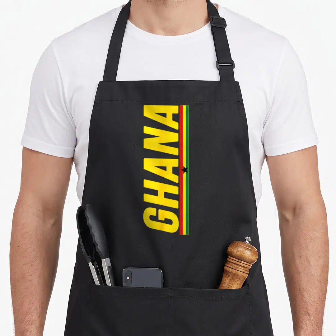 Ghana ghanaian pride apron - Vertical yellow GHANA text beside red green black flag stripe with black star — shown on a black cotton canvas apron against a white background