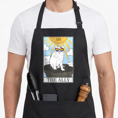 Tarot gay pride apron - Cat in rainbow sunglasses sitting on rock under sun with text XXII THE ALLY — shown on a black cotton canvas apron against a white background