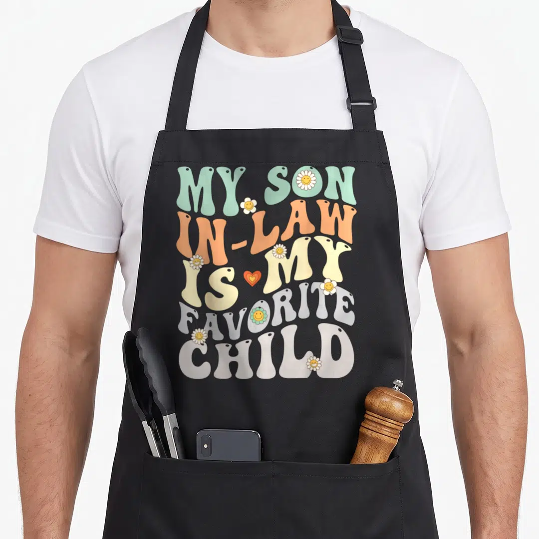 Law son humor apron - Retro bubbly text reading My Son In Law Is My Favorite Child with smiley daisies and a heart — shown on a black cotton canvas apron against a white background