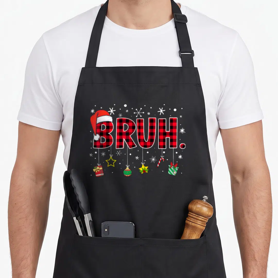 Bruh christmas plaid apron - BRUH text in red plaid with Santa hat, hanging star, candy cane, and gifts surrounded — shown on a black cotton canvas apron against a white background