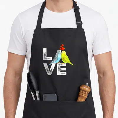 Parrot family aprons - Two budgies kissing over white LOVE text with three red hearts above — shown on a black cotton canvas apron against a white background
