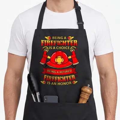 Rescue firefighter cooking apron - Firefighter helmet crossed axes hoses and honor text in red yellow black cartoon — shown on a black cotton canvas apron against a white background