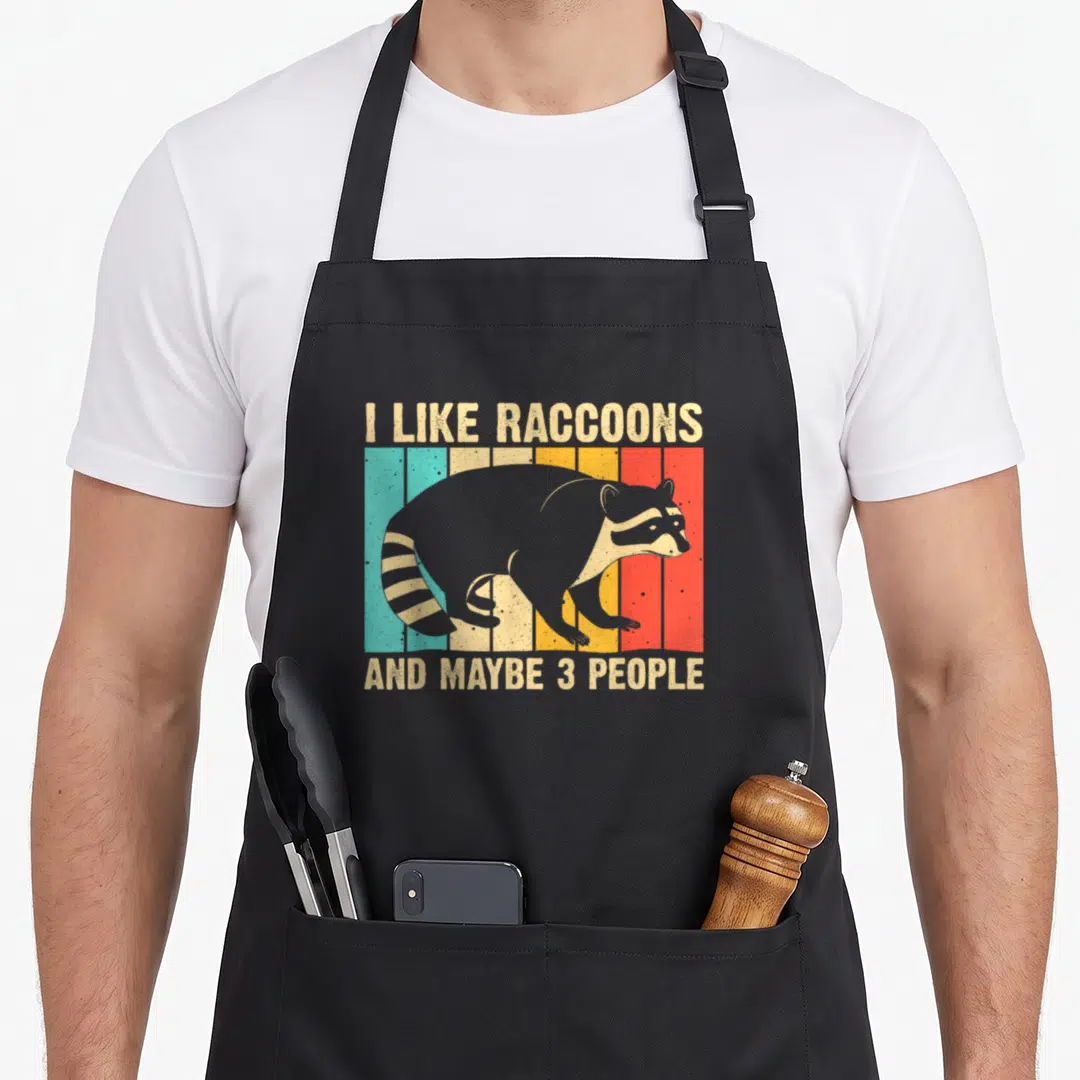Introvert funny raccoon accessories stuff apron - Grey raccoon silhouette over five vertical beige teal yellow orange — shown on a black cotton canvas apron against a white background