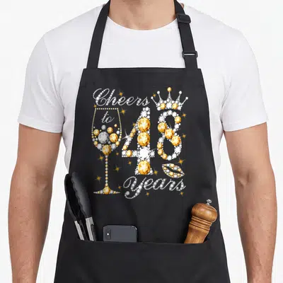 48th wine apron - Diamond style Cheers to 48 years graphic with glass crown and lips in white and gold — shown on a black cotton canvas apron against a white background