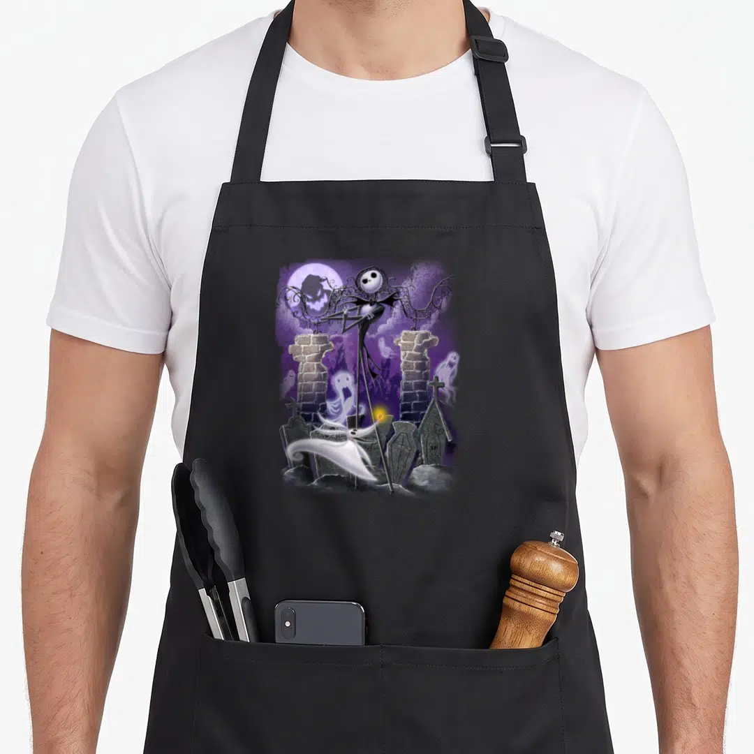 Jack zero apron - Jack Skellington standing in purple graveyard with ghosts and moon — shown on a black cotton canvas apron against a white background