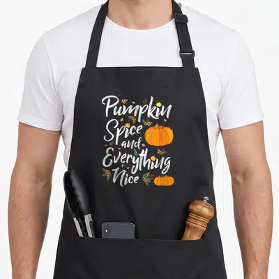 Fall spice apron - Stacked white text reading Pumpkin Spice and Everything Nice surrounded by orange pumpkins — shown on a black cotton canvas apron against a white background