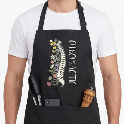 Chiropractor modern apron - Vertical spine with green pink yellow and white flowers and CHIROPRACTIC text — shown on a black cotton canvas apron against a white background