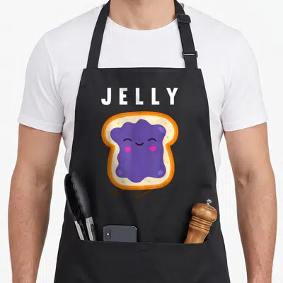 Friend butter apron - Cartoon toast with purple jelly face and white JELLY text — shown on a black cotton canvas apron against a white background