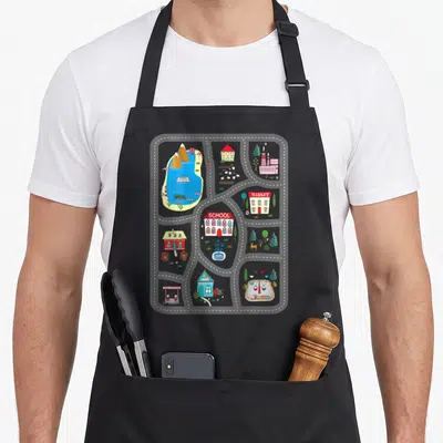 Mat track apron - Cartoon town map with MARKET, SCHOOL, GAS STATION buildings and dashed roads in grey, red, blue — shown on a black cotton canvas apron against a white background