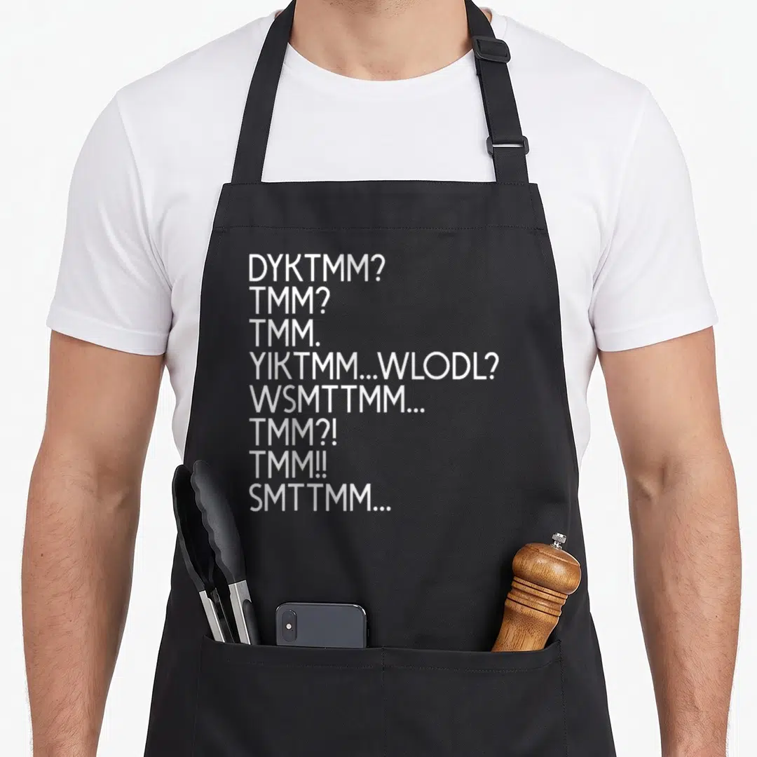 Funny dyktmm muffin man apron - Eight lines of white text including DYKTMM and TMM abbreviations stacked vertically — shown on a black cotton canvas apron against a white background