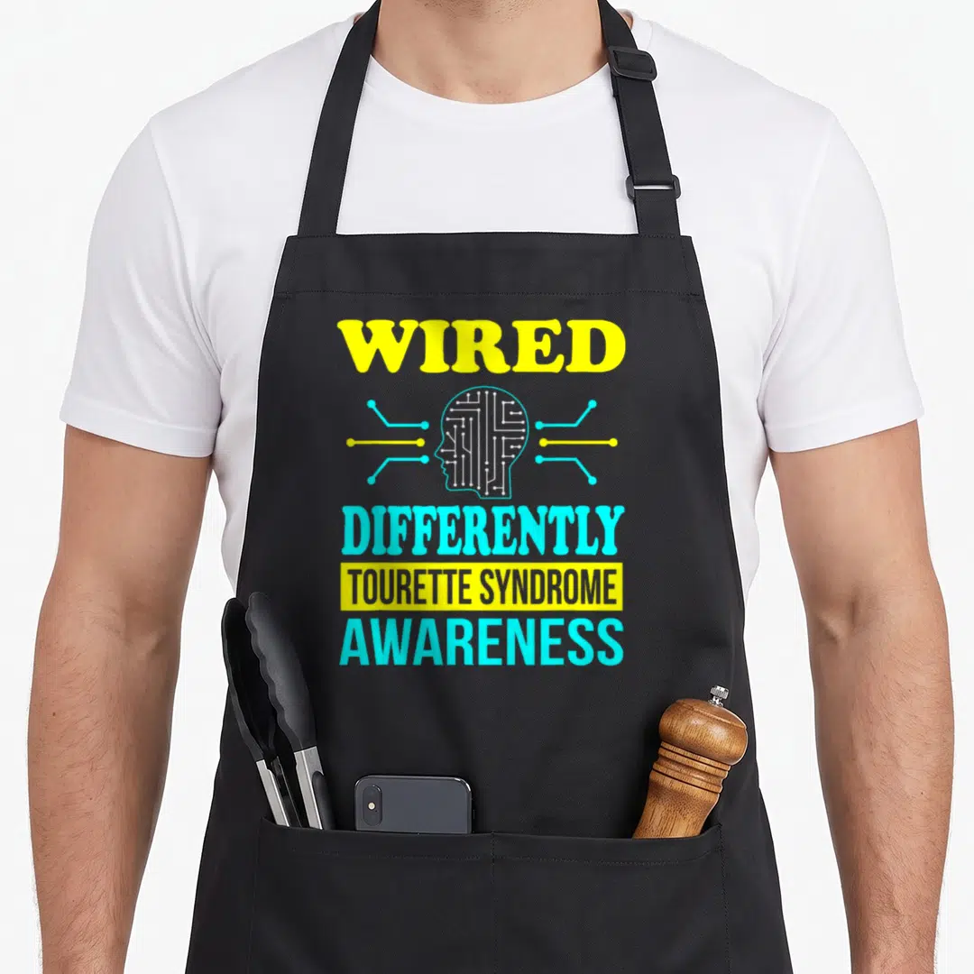 Support tourette awareness apron - Yellow and cyan head with circuit lines and text WIRED DIFFERENTLY TOURETTE SYNDROME — shown on a black cotton canvas apron against a white background
