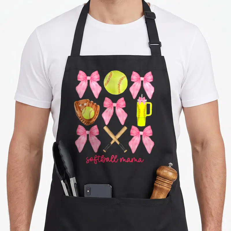 Softball bow apron - Pink bows, yellow softball, brown mitt, crossed bats, and tumbler in a grid layout — shown on a black cotton canvas apron against a white background